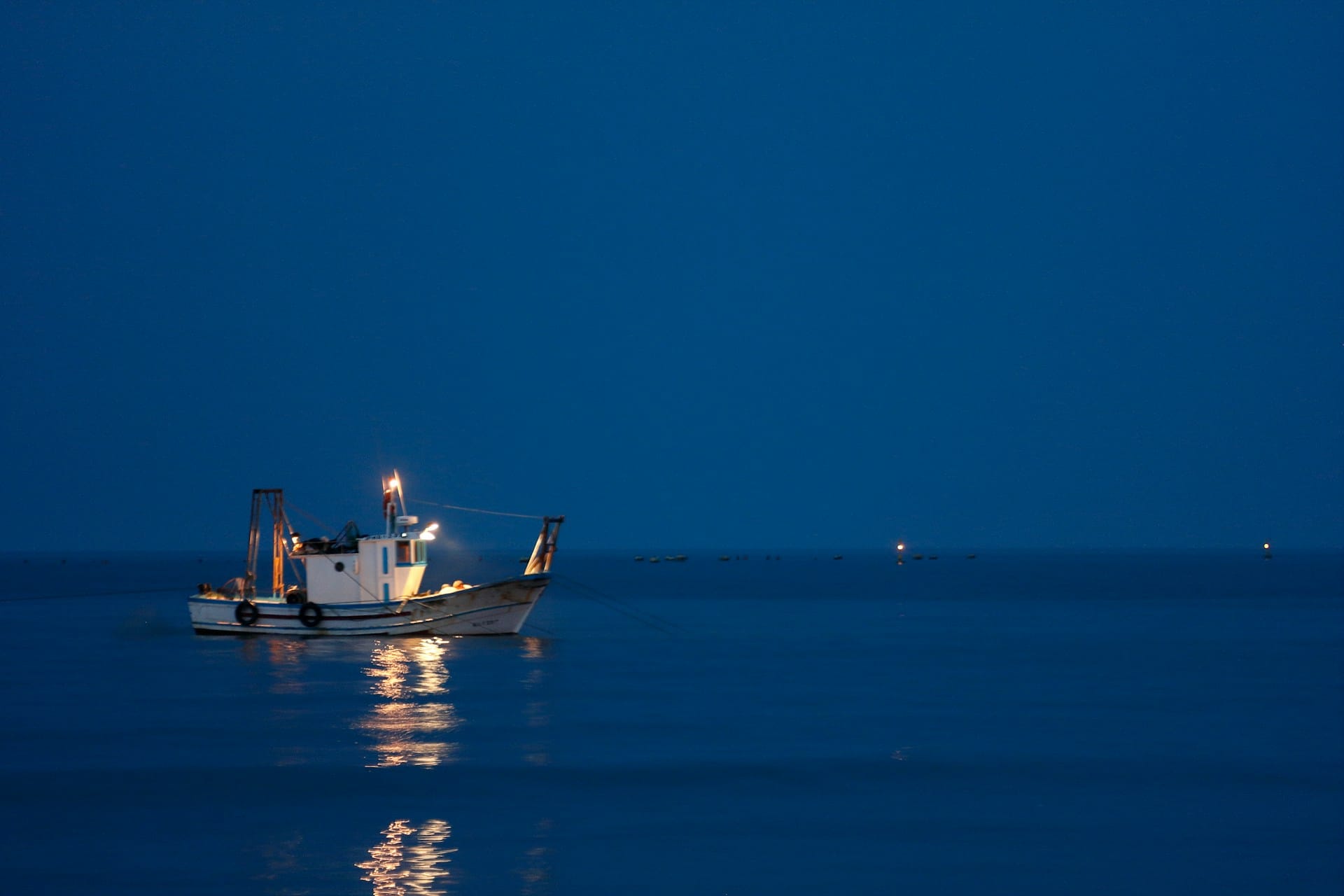 Bote de pesca de noche con sus luces encendidas sobre el agua oscura